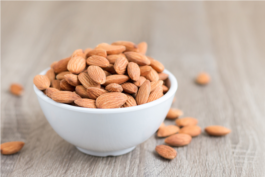 A bowl overflowing with whole, raw almonds, showcasing their natural texture.